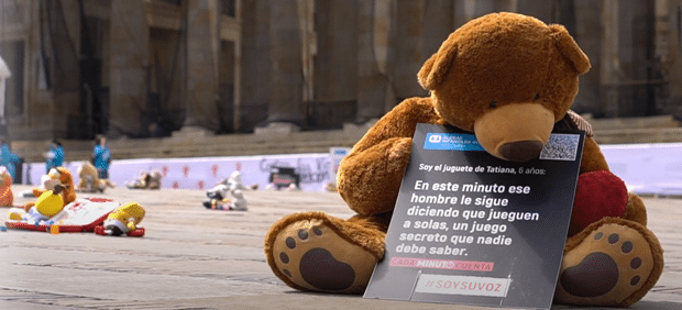 SOS-barnebyer og bamsekampanjen. Bamser spredt på gaten i Colombia for å understreke voldutsatte barn, hvor bamsene snakker på vegne av barna. Foto: Daniel Castaño Leal. En brun bamse sitter på et fortau og holder en plakat. Foto: SOS-barnebyer Colombia