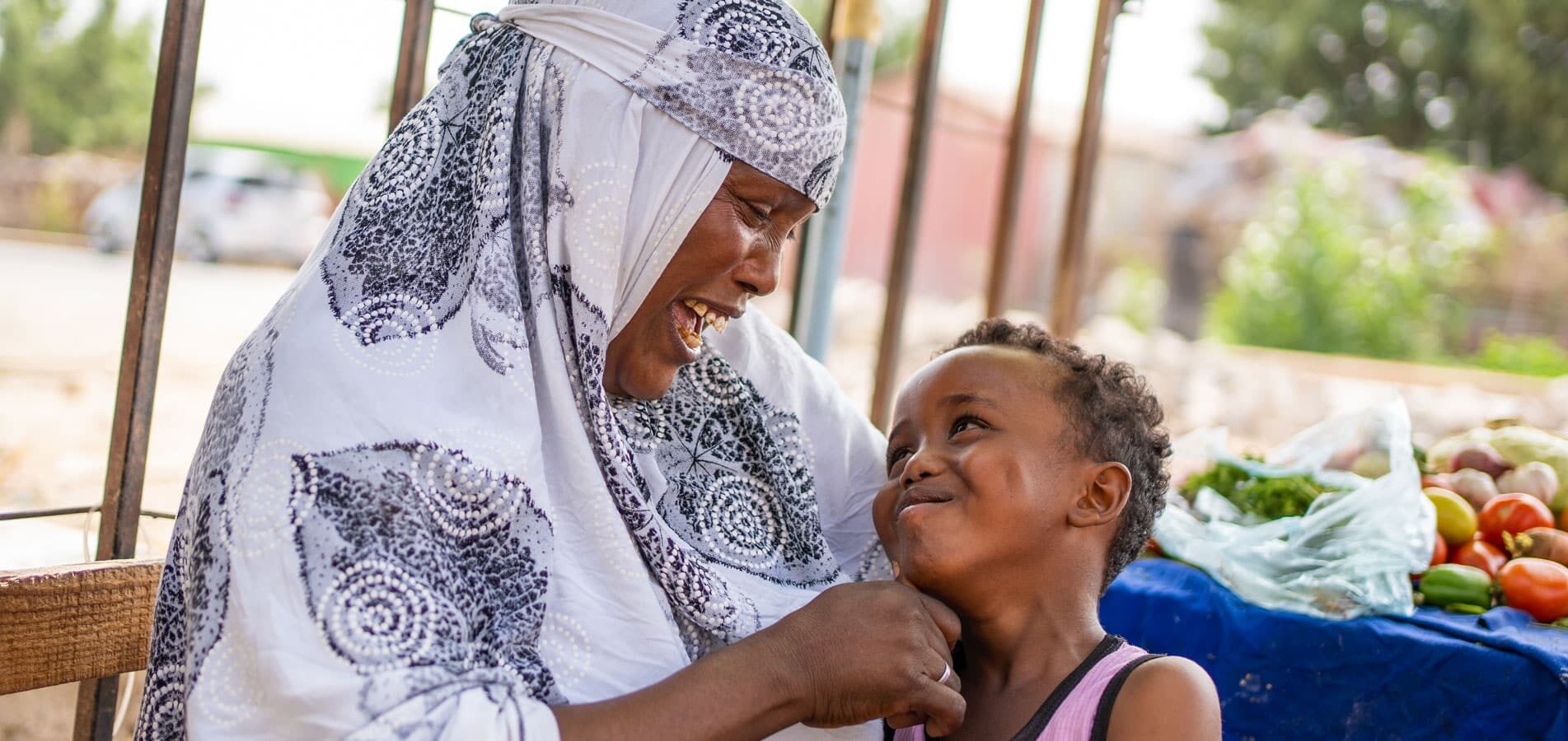 Somaliland: Mor i hvit mønstret hijab har sønnen på fanget. han har rosa singlet og smiler opp til henne. Hodans familie har fått støtte gjennom SOS-barnebyers forebyggende arbeid. Foto: Lydia Mantler