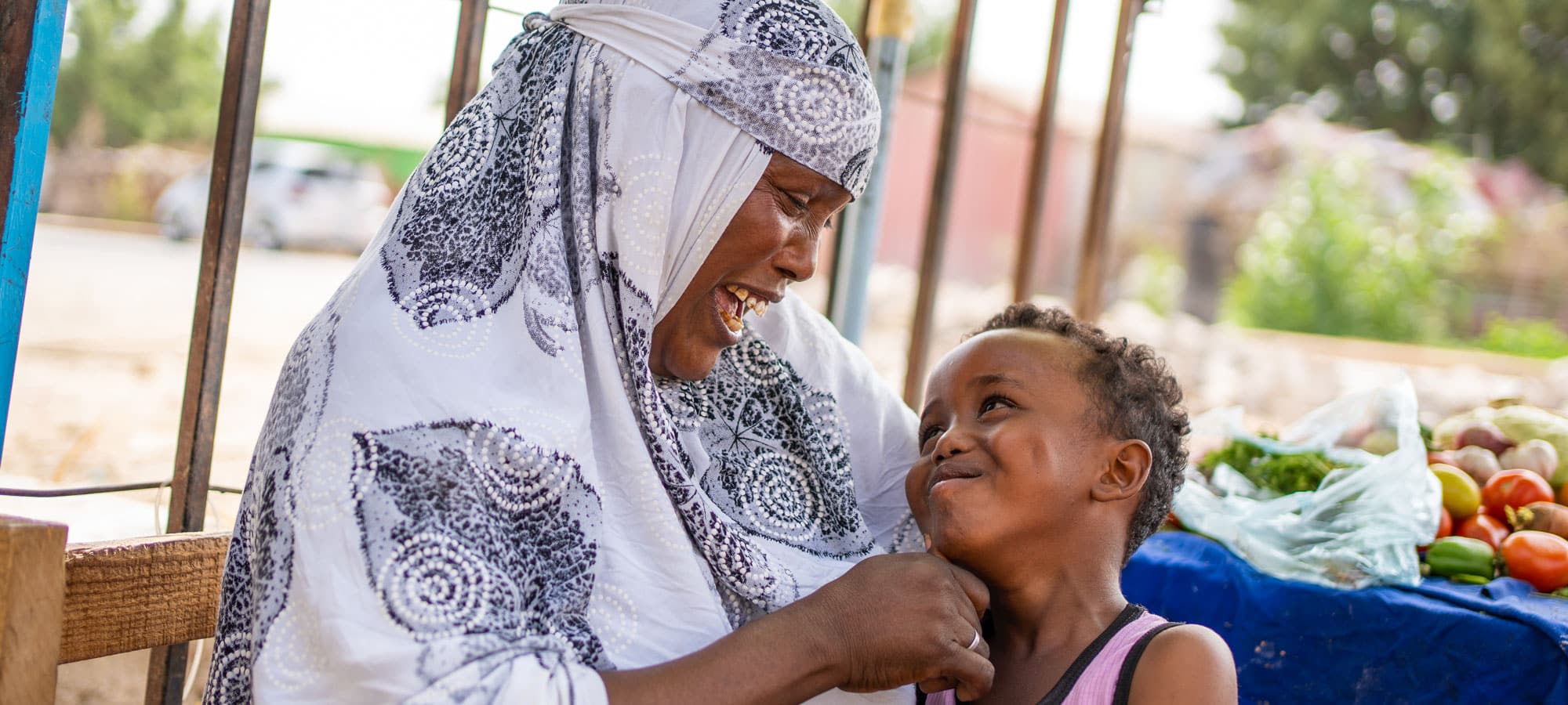 Somaliland: Mor i hvit mønstret hijab har sønnen på fanget. han har rosa singlet og smiler opp til henne. Foto: Lydia Mantler