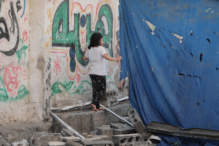 Ei jente alene i ruinene i Gaza. Hun har halvlangt mørkt hår, hvit t-skjorte og mønstrete bukse. Foto: Hosny Salah