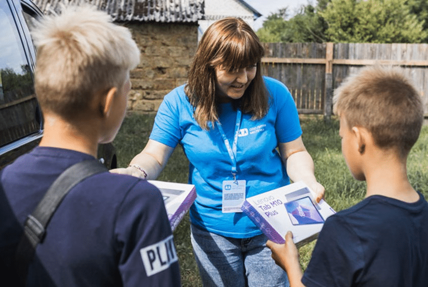 Medarbeider fra SOS-barnebyer i Ukraina med blå t-skjorte med vår logo deler ut bøker til to gutter som står med ryggen til. Begge gutta har mørkeblå t-skjorter. Foto Ksenia Borisova