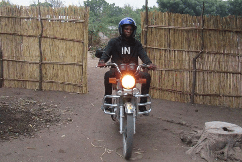 Yohane med blå hjelp og blå hettegenser sitter på motorsykkelen sin. Foto: SOS-barnebyer