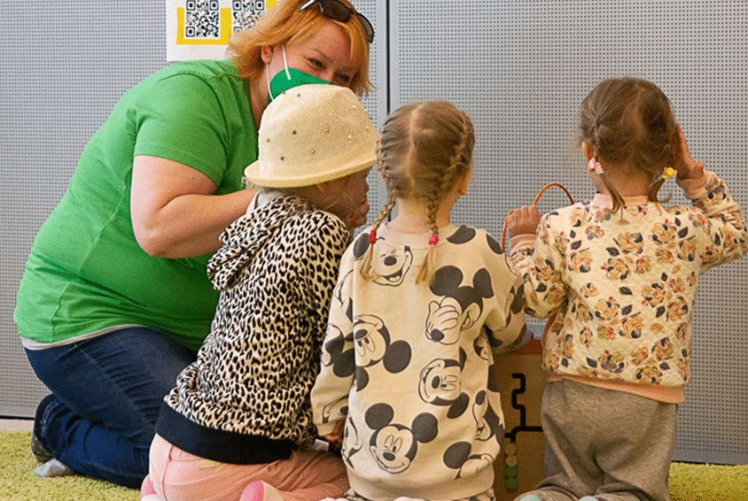 Tre jenter siter på knærne med ryggen til kamera og snakker med en sosialarbeider fra SOS-barnebyer. foto Alexandra Terr