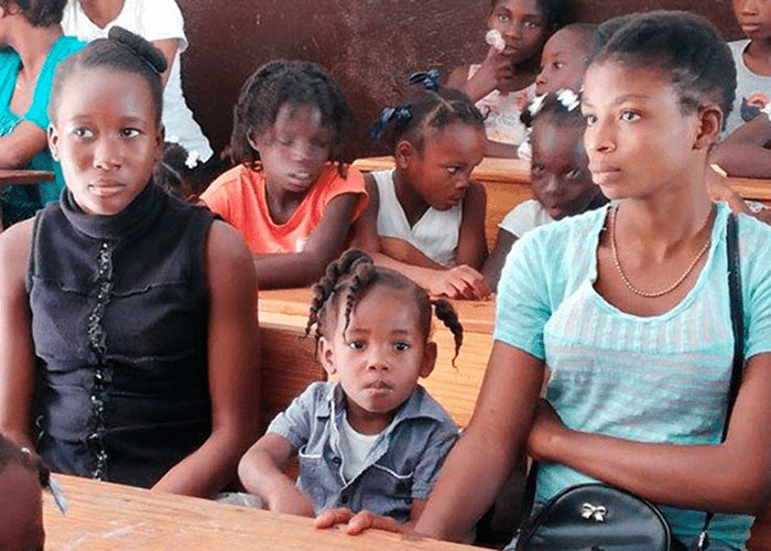 To tenåringsjenter og ei lita jente sitter ved en skolepult i ett barnevennlig senter. Foto: SOS-barnebyer Haiti