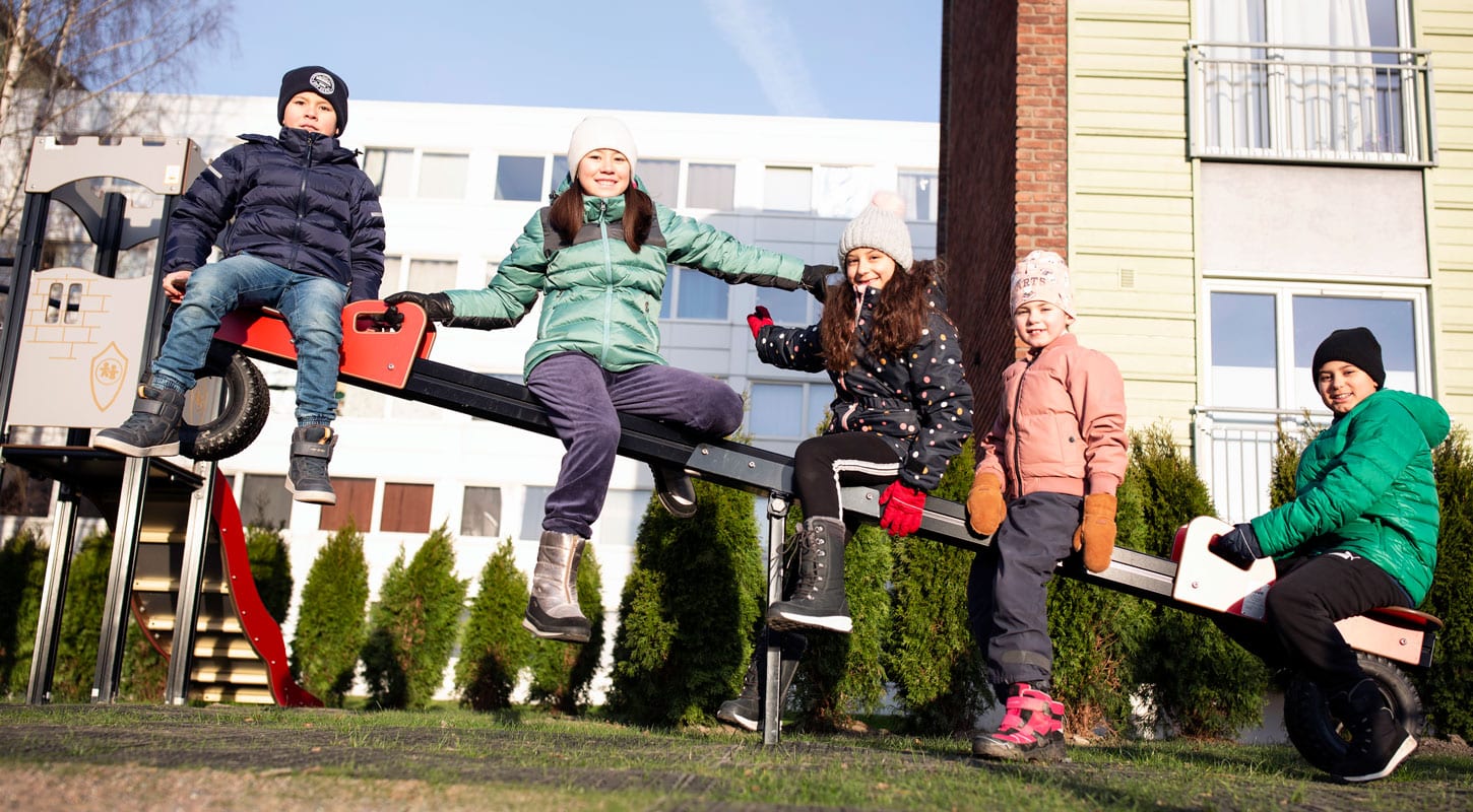 Fem barn sitter på ei dumphuske. De har tykke jakker og luer. I bakgrunnen er det et lekeapparat og blokker. Foto: Lillian Hjellum