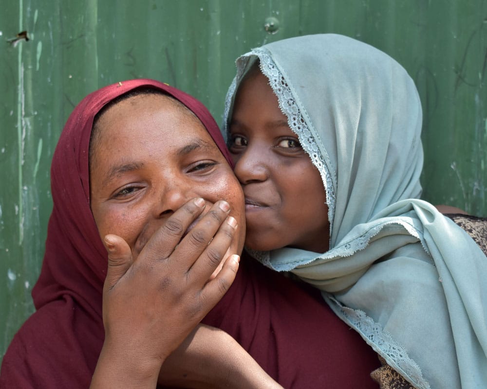 Tashi, men lys blå hijab og mønstrete svart og hvit kjole, gir moren, i rød hijab en god klem. Foto: Christine Stoltz