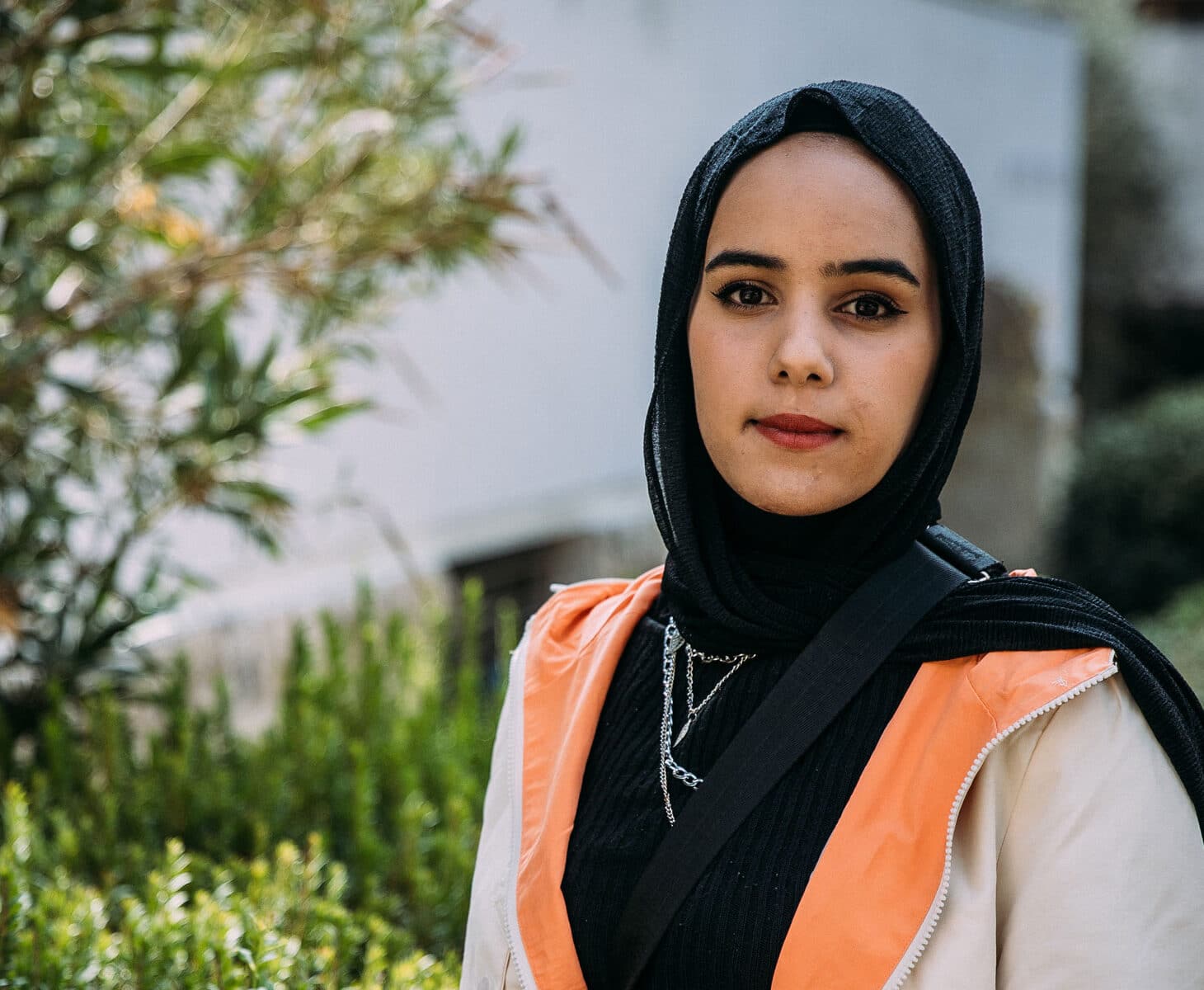 Portrett av Haneen som står ute og som smiler, hun har på seg svart genser, beige jakke og hijab. Foto: Alea Horst