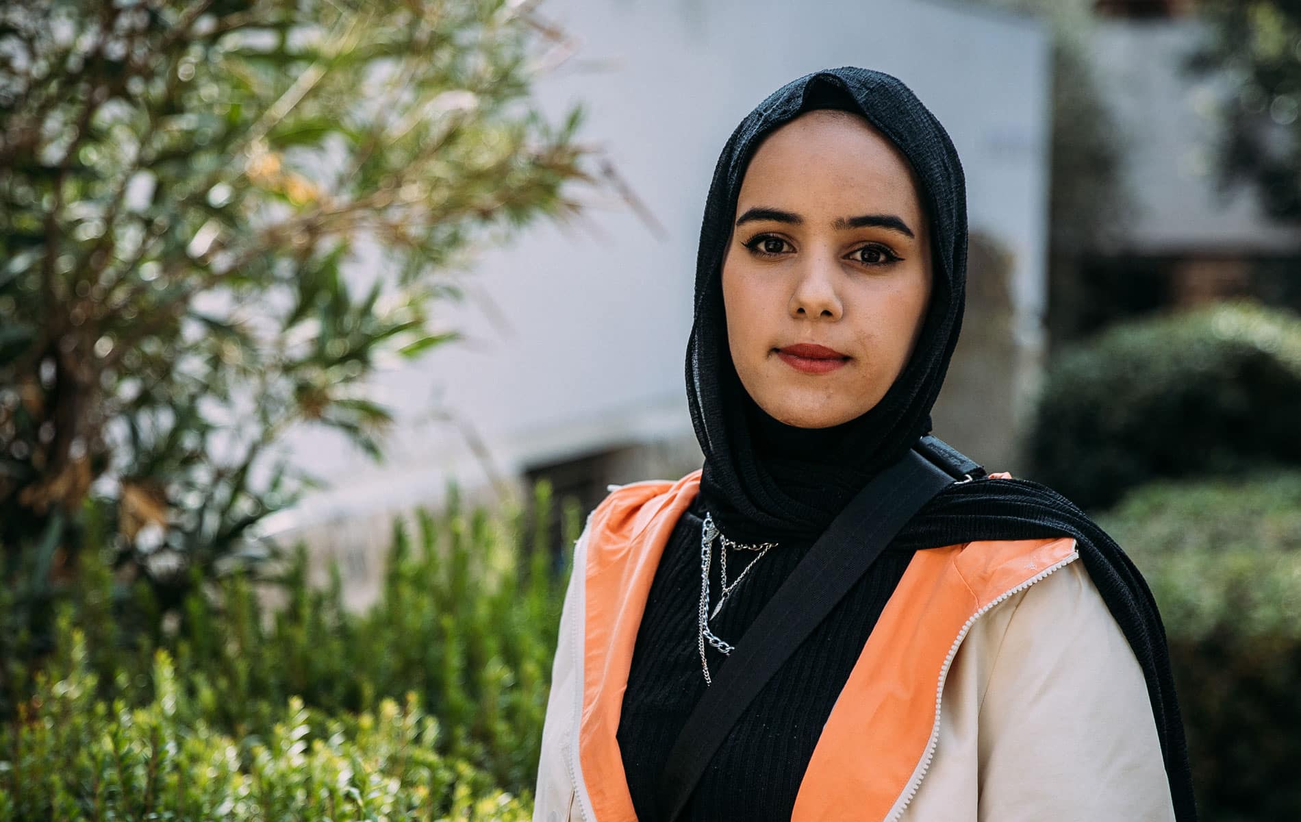 Portrett av Haneen som står ute og som smiler, hun har på seg svart genser, beige jakke og hijab. Foto: Alea Horst