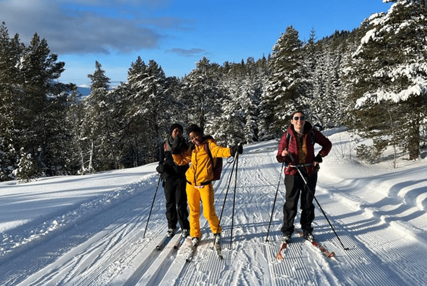 Elena med knall gul skidress står i løypa sammen med to andre studenter. Været er strålende. Foto: Privat