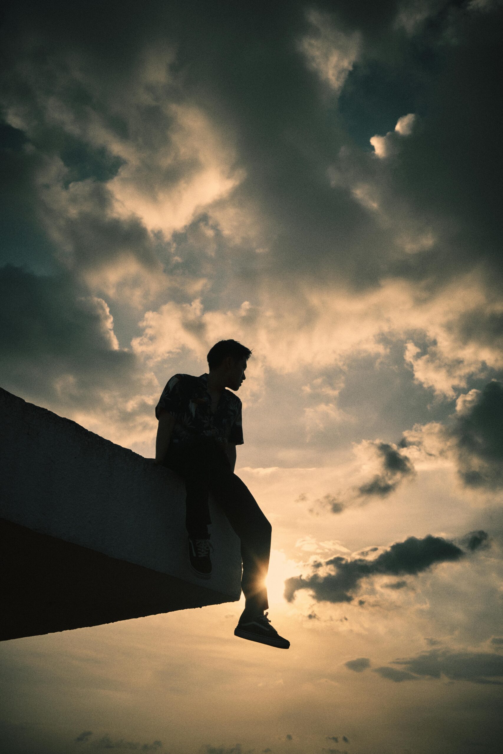 Den svarte siluetten av en ung man som sitter på et stupebrett mens han ser utover sjøen. Foto Pexels Khoa Vo