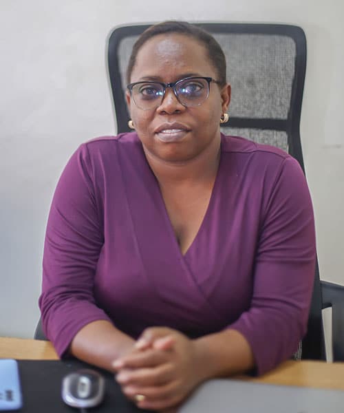 Beatrice Mutamuliza, sosialarbeider for SOS-barnebyer i Kigali, sitter på kontoret med hendene lent på pulten foran seg. Hun har kort hår, briller og lilla kjole. Foto: SOS-barnebyer