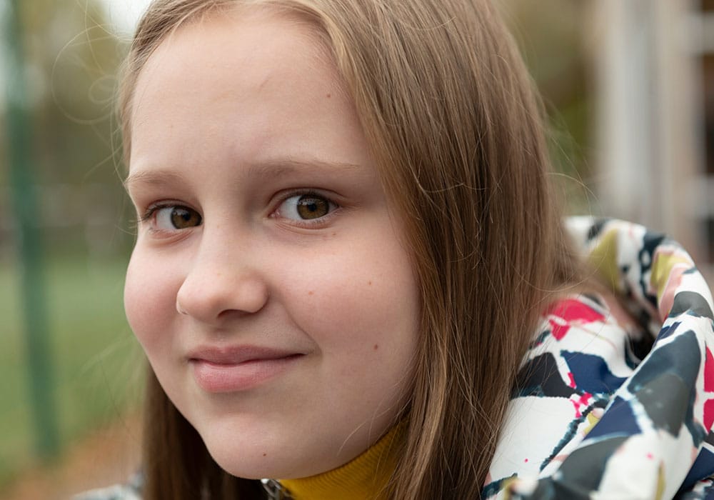 Sofiya, med langt, blondt hår, og mønstrete jakke med hette, smiler. Foto: Katerina Ilievska
