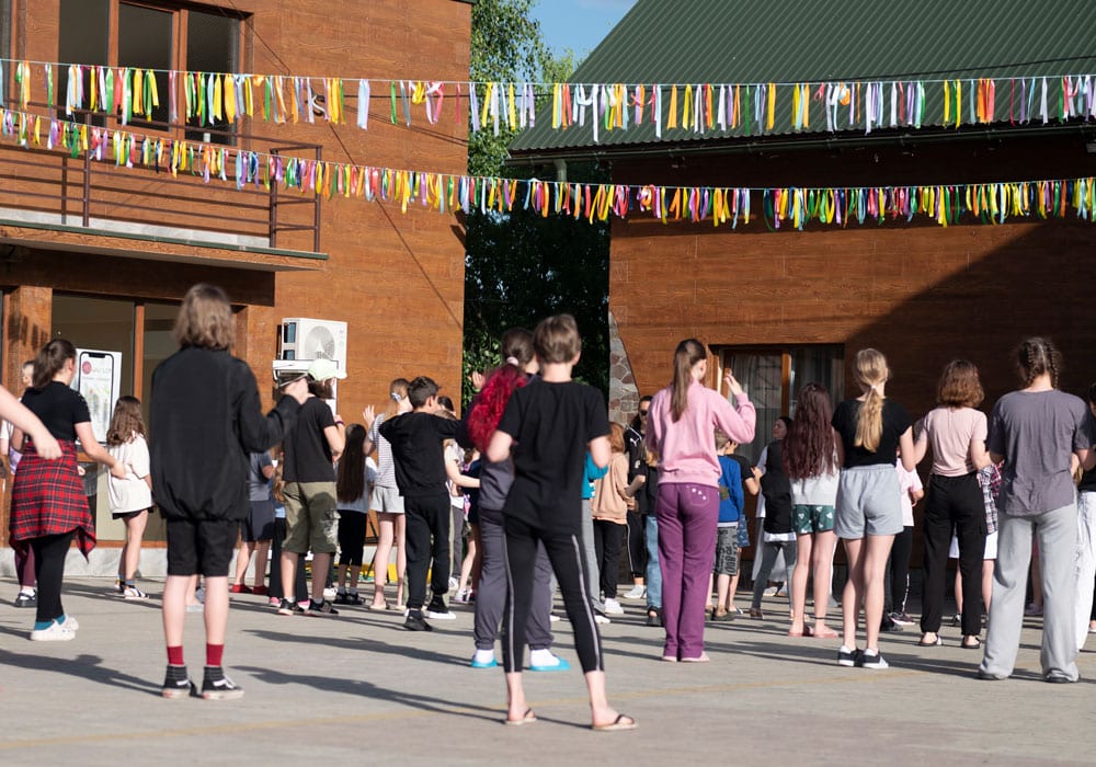 En gruppe barn og unge står ute og danser, over dem henger det fargerike girlander. Foto: Katerina Ilievska