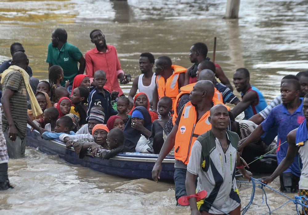 Flommen i Nigeria: Barn og mødrene deres sitter i en overfylt båt på ei flomstor elv. Flere menn med vann til livet drar båten. Foto Audu Marte AFP
