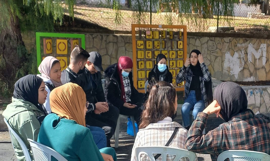 Unge kvinner og menn sitter ute på stoler og snakker sammen. Foto SOS-barnebyer Palestina